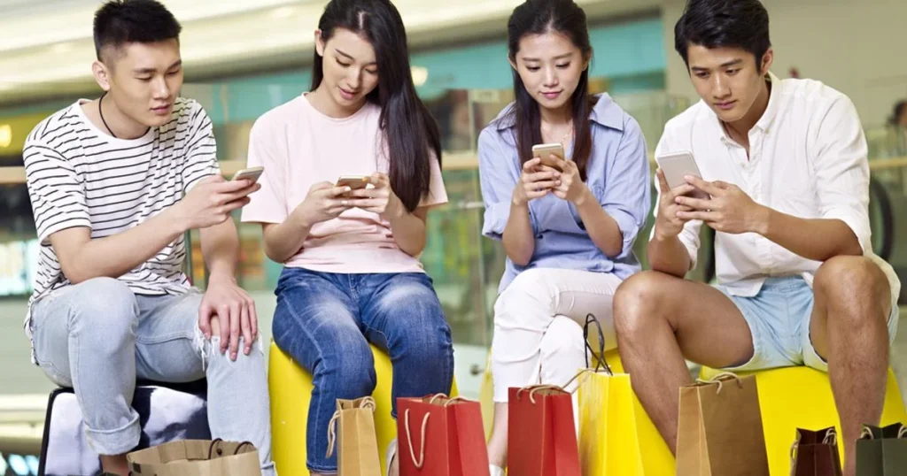 Chinese Gen Z consumers sitting with shopping bags while browsing products on smartphones in a mall