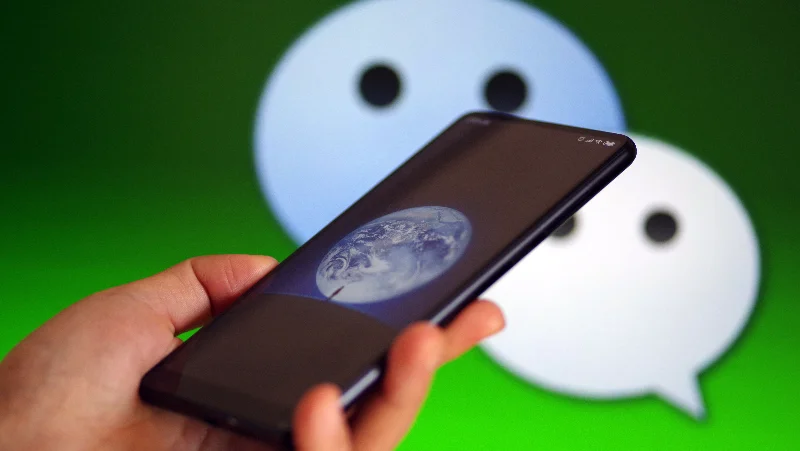 Smartphone held in hand with WeChat logo in the background, representing how users interact with external links and content inside the WeChat ecosystem