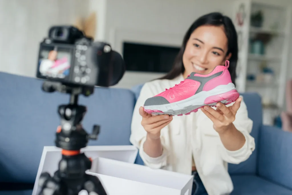 Content creator holding a pink sneaker in front of a camera while recording a product review for online shoppers.