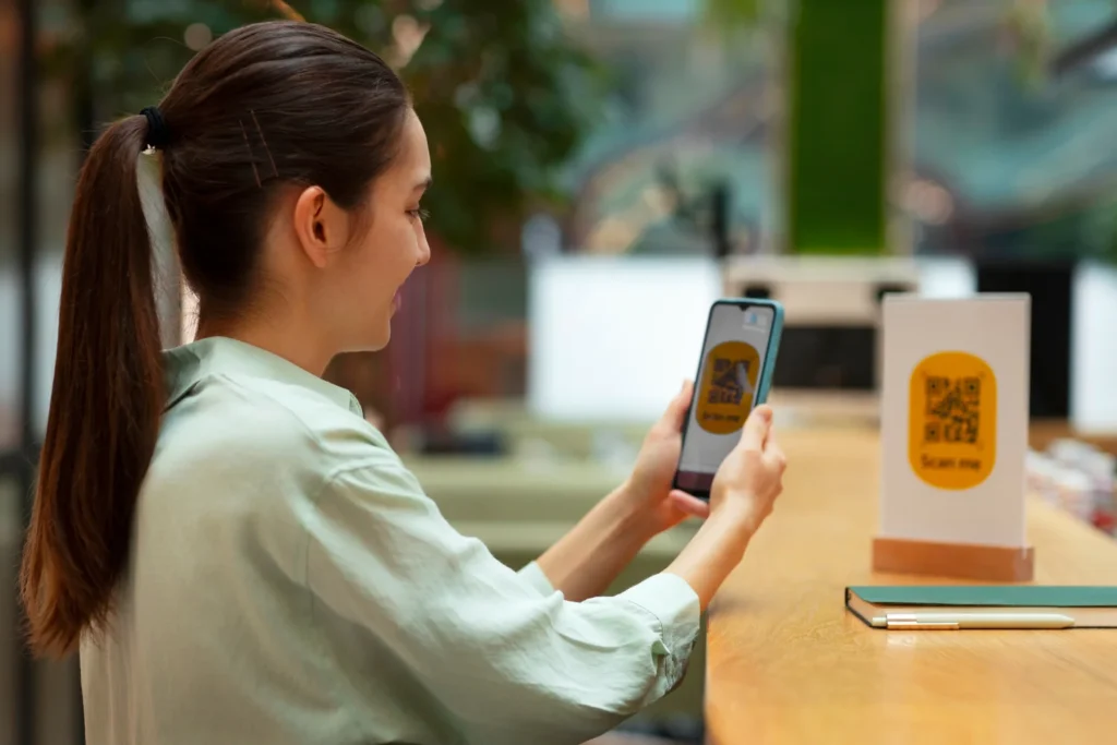 Woman scanning a QR code with her smartphone at a counter, illustrating mobile payment and digital checkout.