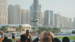 XPeng flying car performing public demonstration flight over Dubai skyline with audience recording urban air mobility test