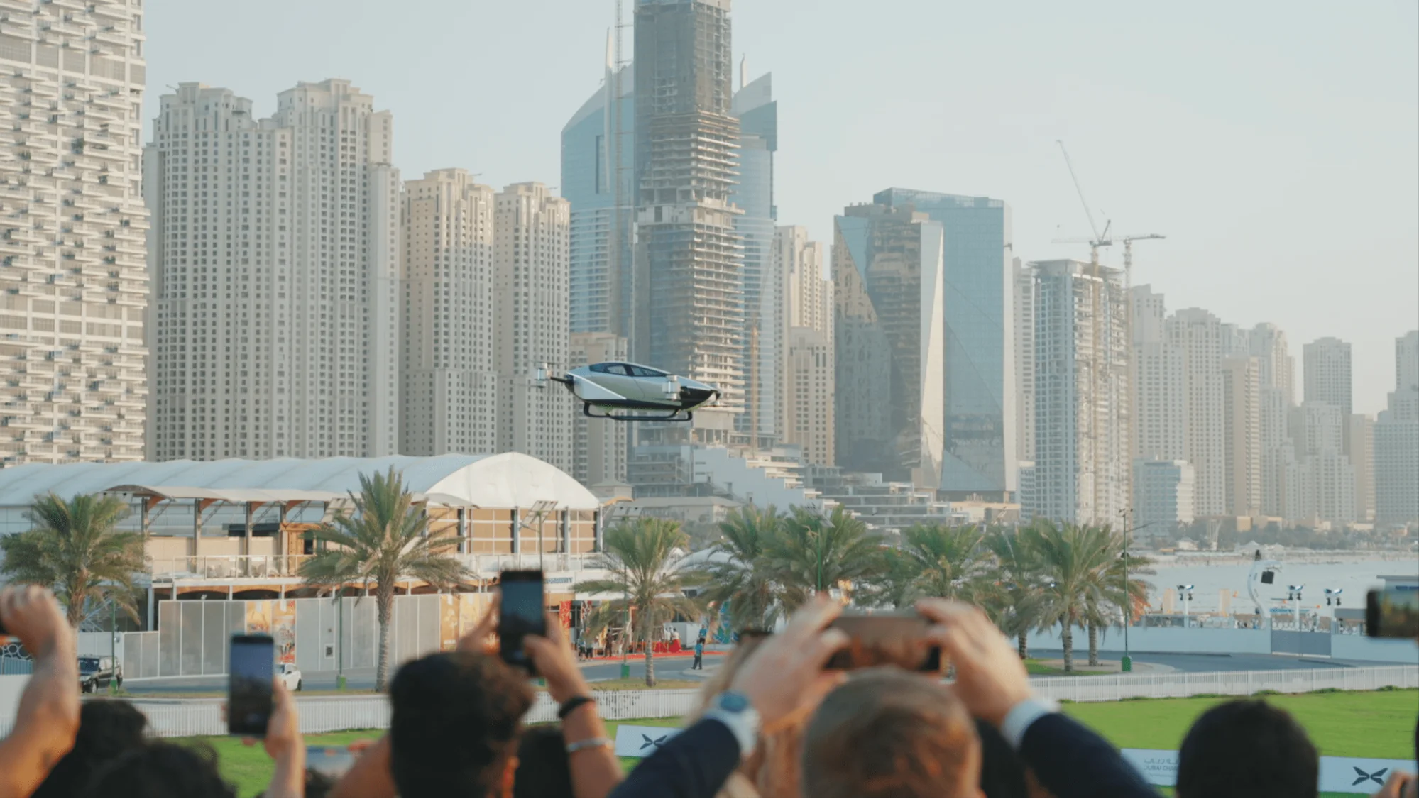 XPeng flying car performing public demonstration flight over Dubai skyline with audience recording urban air mobility test