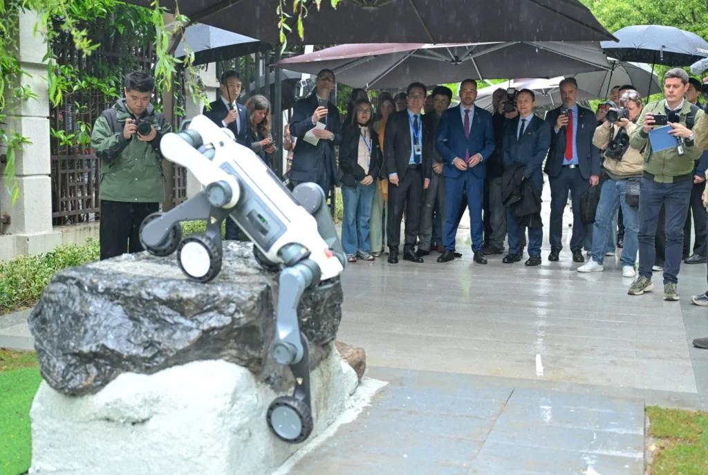 Quadruped robot climbing obstacle during live demonstration with audience observing outdoors