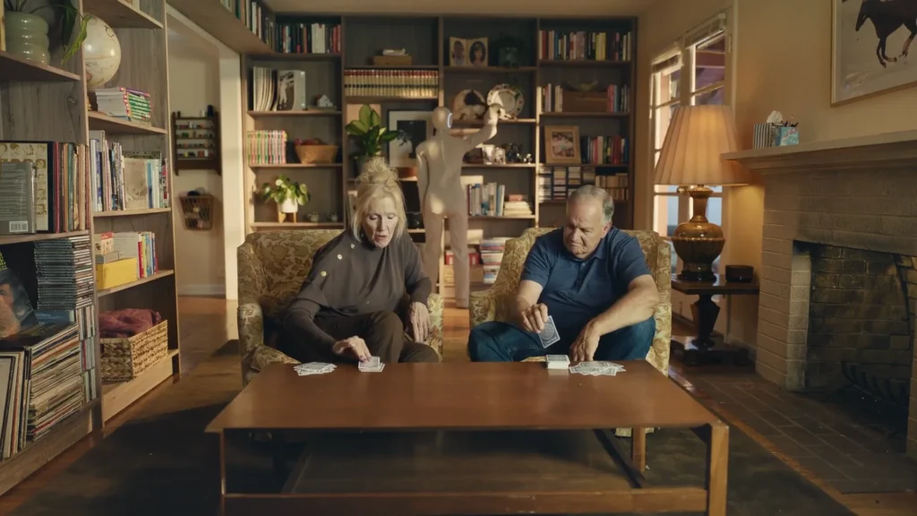 Elderly couple playing cards while the NEO home robot organizes shelves in the background