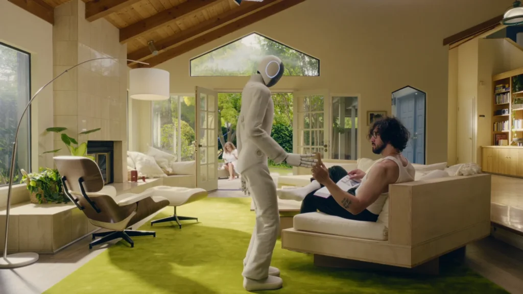 1X NEO humanoid robot handing a drink to a man inside a bright modern living room
