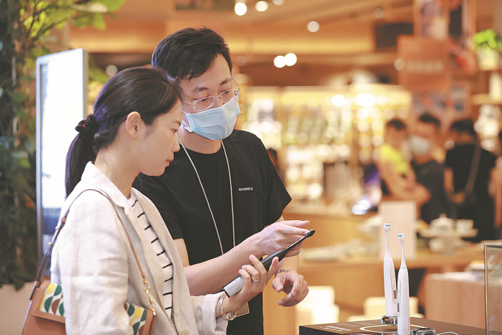 A retail representative demonstrates a smart electric toothbrush product to a shopper inside a modern Chinese retail store.