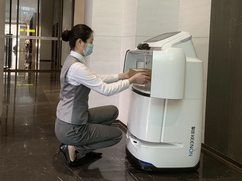 Hotel worker placing items into a Keenon service robot for delivery