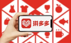 Hand holding smartphone displaying Pinduoduo app logo with shopping category icons in background