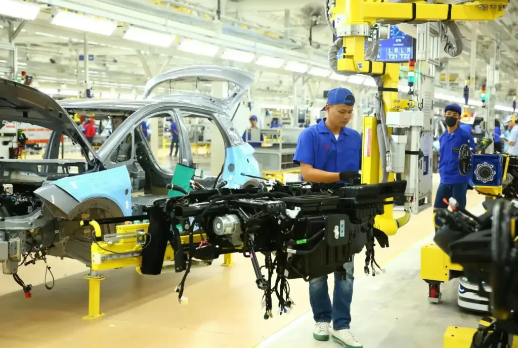 Factory workers assembling car chassis with robotic assistance