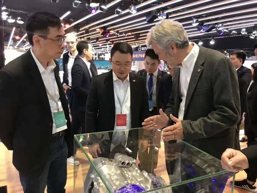 Group of professionals examining engine technology display at an automotive exhibition.
