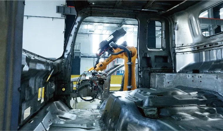 Industrial robotic arm performing welding inside car body assembly line.