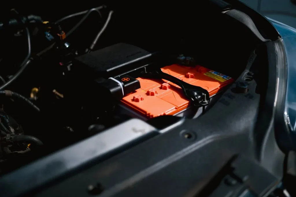 Orange car battery installed inside a vehicle engine bay.