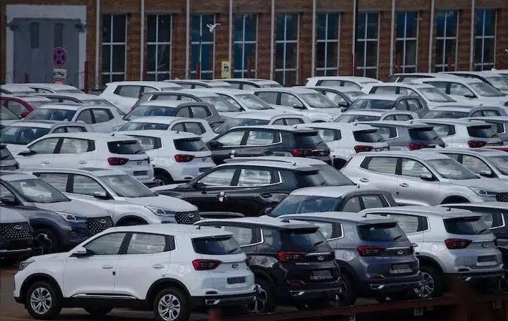 Large parking lot filled with Chery cars lined up in rows outside a factory or storage yard.