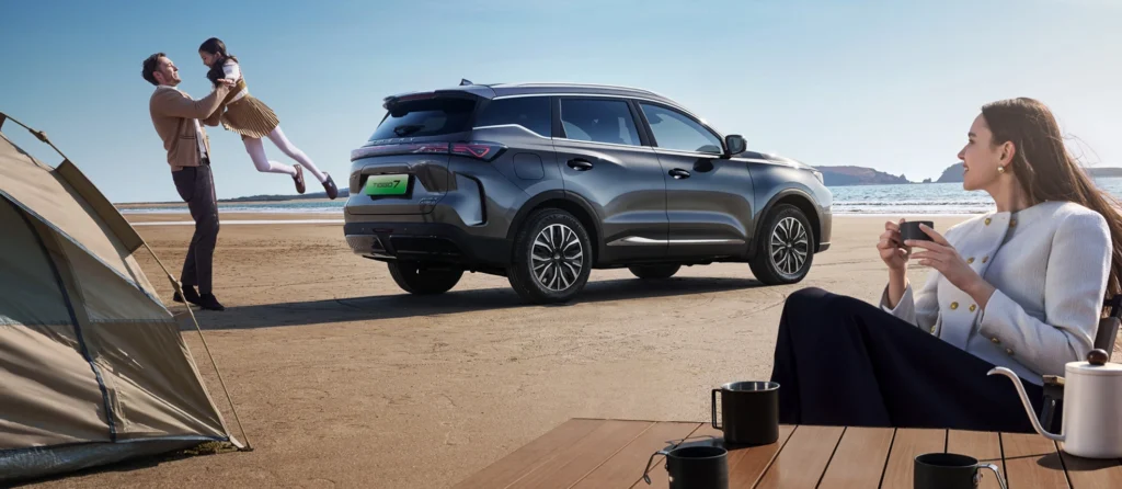 Chery SUV on a beach setting with a family scene beside tents and ocean background.