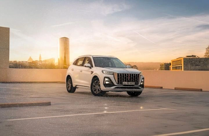 White Hongqi SUV driving on an open road during sunset with city skyline in background.