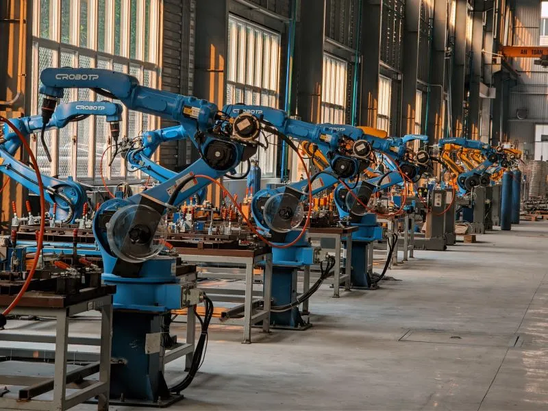 Multiple blue industrial robotic arms working in a factory automation assembly line.