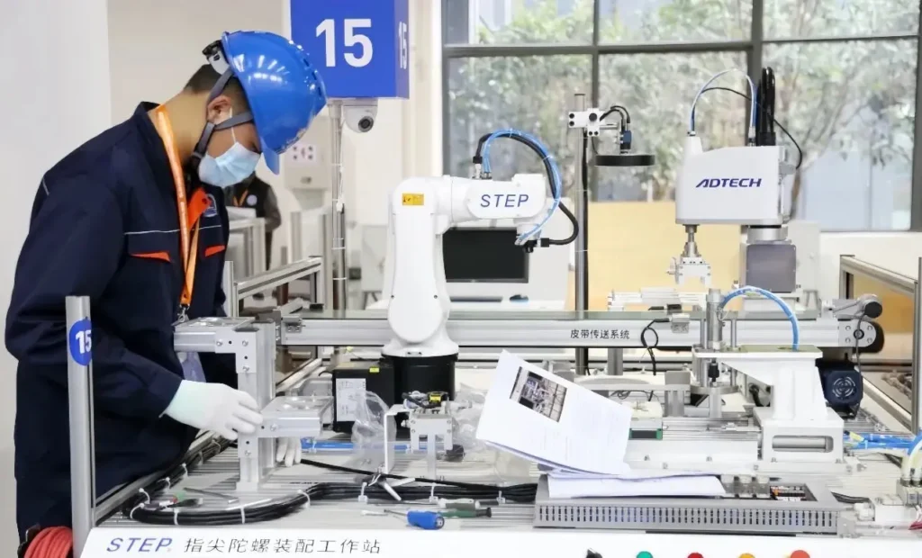 Worker operating STEP industrial robot assembly station with automated equipment and safety gear.
