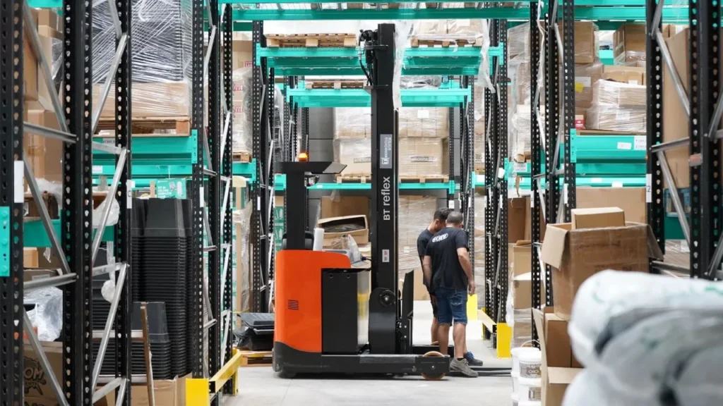 Warehouse aisle with forklift and workers near storage racks