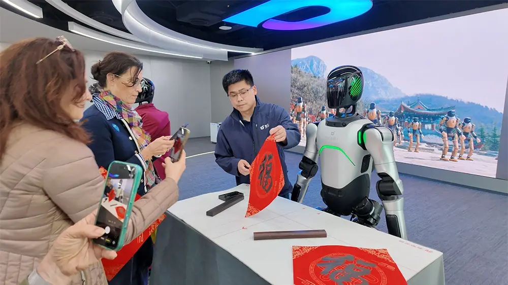 Visitors watch a guide demonstrate an activity beside a silver humanoid robot.