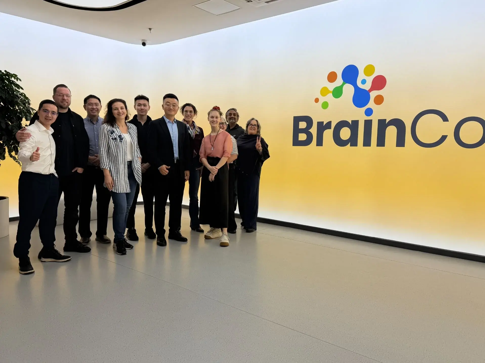A visiting group stands beside the BrainCo logo in a company lobby.