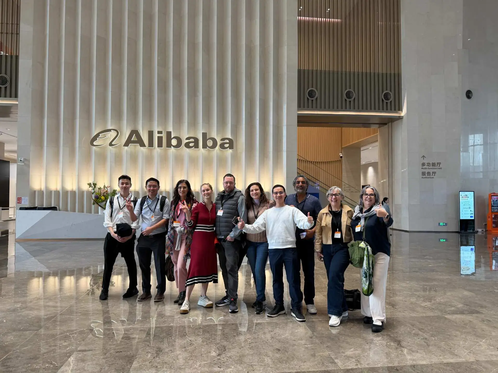 A visiting group poses in a lobby beneath the Alibaba logo.